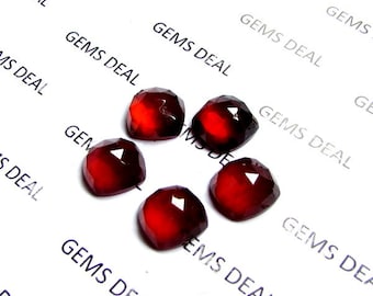 Puede incluir: Seis cabujones de piedras preciosas rojas, cada uno con una forma cuadrada facetada. Las piedras están dispuestas en círculo sobre un fondo blanco con el texto "GEMS DEAL" impreso en el fondo.