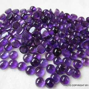 May include: A large pile of round, purple amethyst cabochons. The cabochons are smooth and polished, with a deep purple color.