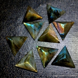 Könnte beinhalten: Neun schimmernde grüne, blaue und goldene Labradorit-Pyramidenkristalle auf einer dunkelgrauen Oberfläche.