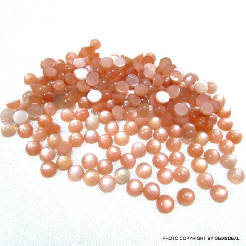 May include: A large pile of round, peach-colored sunstone cabochons. The stones have a shimmery, iridescent finish.