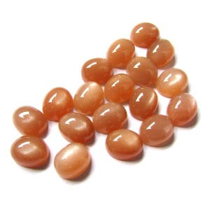 May include: A collection of 18 oval-shaped, peach-colored sunstone cabochons. The stones have a shimmery, iridescent quality.