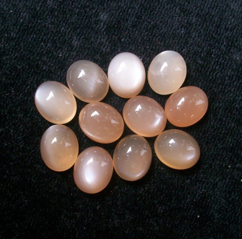 May include: A collection of 10 oval-shaped moonstone cabochons in various shades of white and peach.