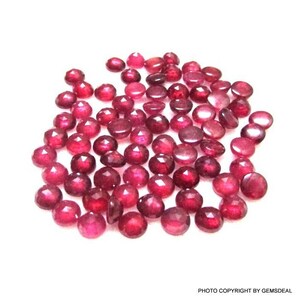 Puede incluir: Un montón de piedras preciosas redondas de rubí rojo. Las piedras preciosas son facetadas y tienen un acabado brillante y pulido.