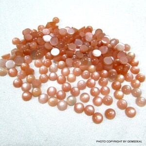 May include: A pile of round, peach-colored sunstone cabochons. The stones have a shimmery, iridescent quality.