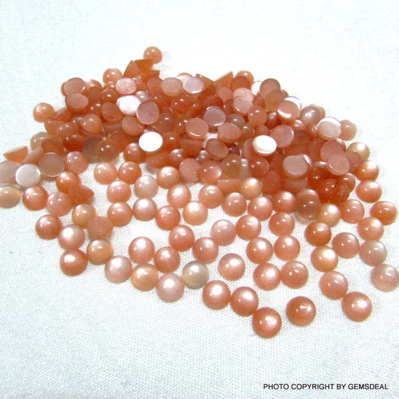 May include: A pile of round, peach-colored sunstone cabochons. The stones have a shimmery, iridescent quality.
