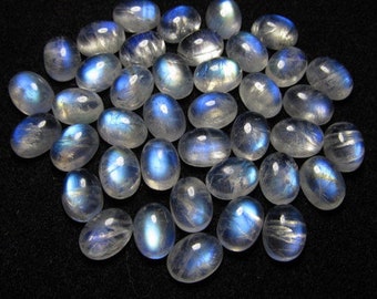 May include: A collection of oval-shaped moonstone cabochons, with a milky white color and iridescent blue flashes.