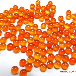 May include: A large group of round, orange carnelian gemstones. The gemstones are smooth and polished, with a slight variation in color.