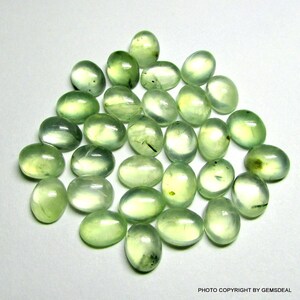 May include: A collection of 25 oval-shaped green gemstones. The stones are smooth and polished, with a translucent appearance.