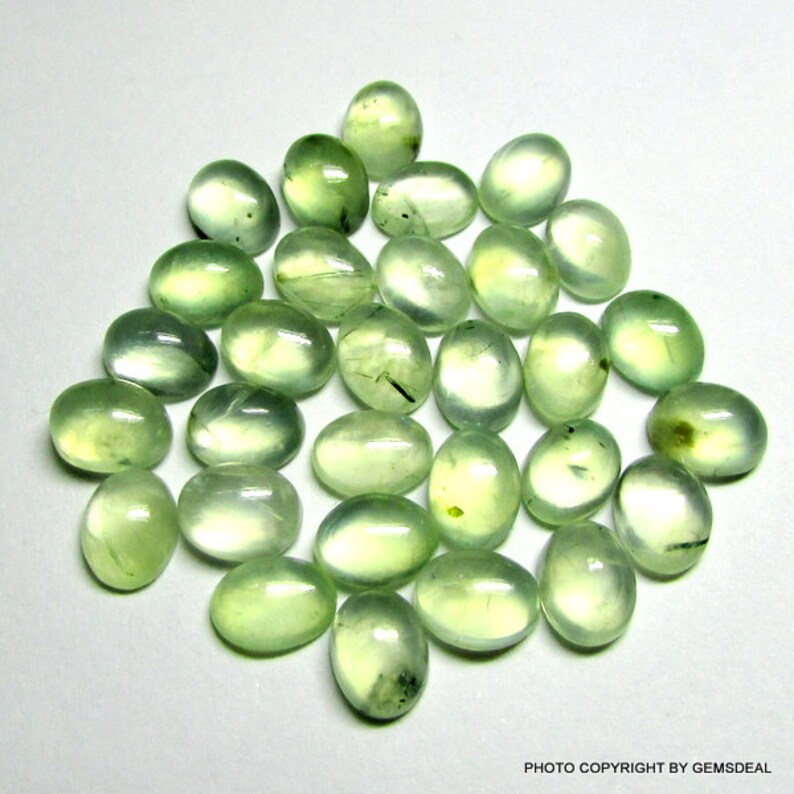 May include: A collection of 25 oval-shaped green gemstones. The stones are smooth and polished, with a translucent appearance.
