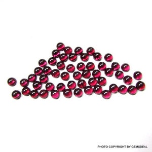 May include: A group of 40 round, red gemstone cabochons. The cabochons are smooth and polished, with a slight shine. They are arranged in a loose, flowing pattern.