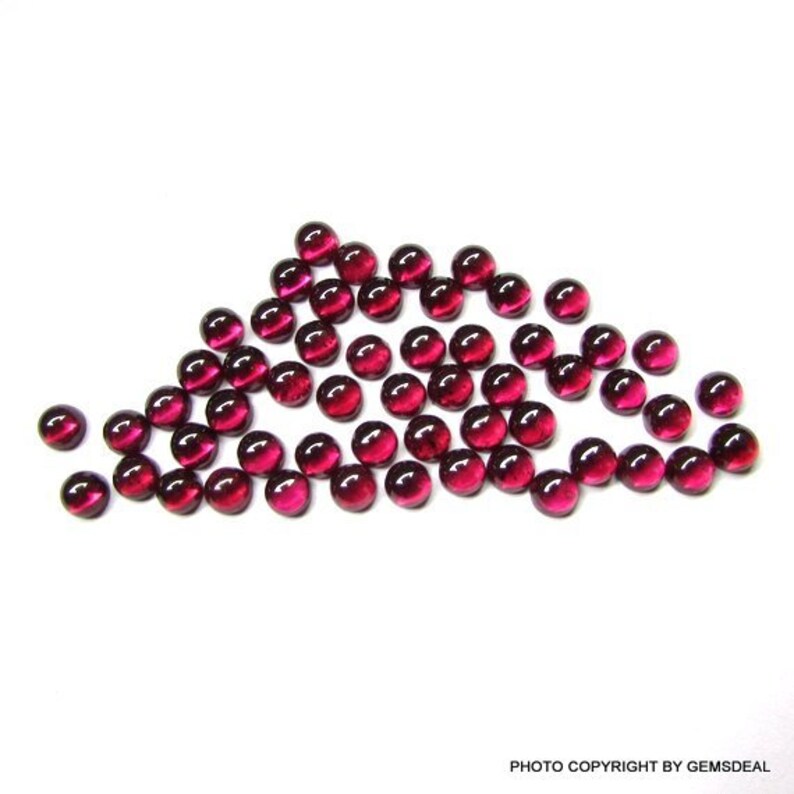 May include: A group of 40 round, red gemstone cabochons. The cabochons are smooth and polished, with a slight shine. They are arranged in a loose, flowing pattern.