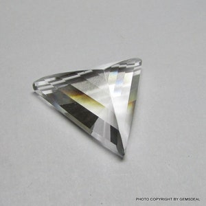 Può includere: Un cristallo triangolare trasparente e sfaccettato con un effetto arcobaleno. Il cristallo è tagliato a forma di piramide con più sfaccettature.