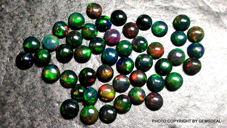 May include: A collection of 40 round, black opal cabochons with green, red, and blue iridescent flashes. The opals are approximately 6mm in diameter.