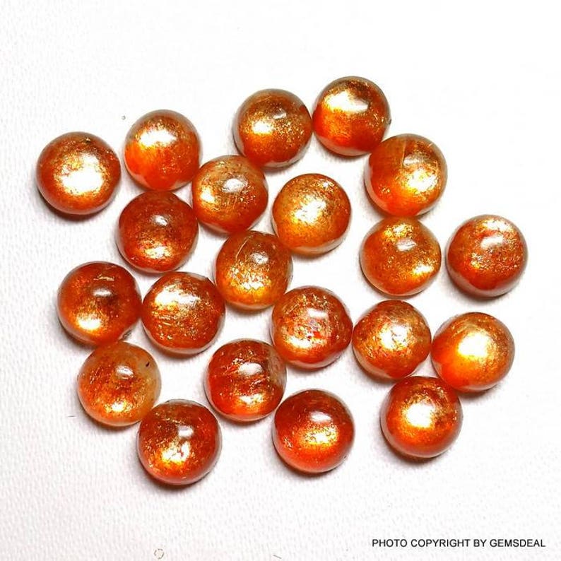 May include: A collection of 20 round, orange sunstone cabochons. The stones have a shimmery, iridescent finish.