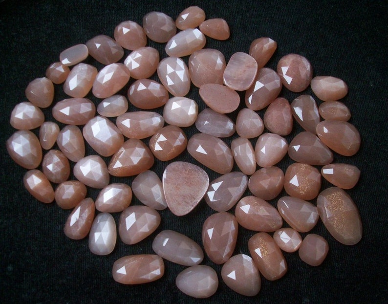 May include: A collection of approximately 40 sunstone gemstones, each with a unique, faceted shape. The stones are a pale peach color with a subtle shimmer.
