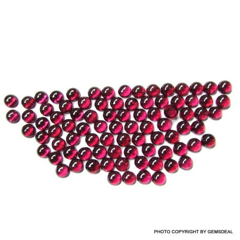 May include: A collection of round, red gemstones, likely rubies, arranged in a loose, flowing pattern. The gemstones are smooth and polished, with a high shine.