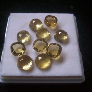 May include: Ten faceted, cushion-cut, yellow gemstones displayed in a white box. The gemstones are arranged in a circular pattern.