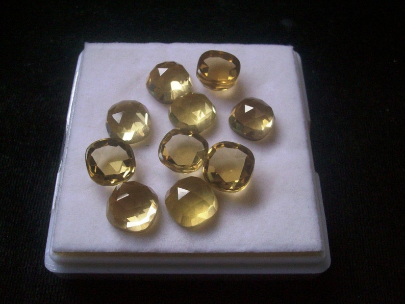 May include: Ten faceted, cushion-cut, yellow gemstones displayed in a white box. The gemstones are arranged in a circular pattern.