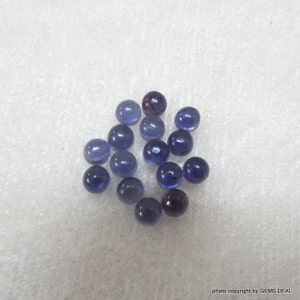 May include: A collection of 16 round, smooth, blue gemstones. The gemstones are scattered on a white, textured surface.
