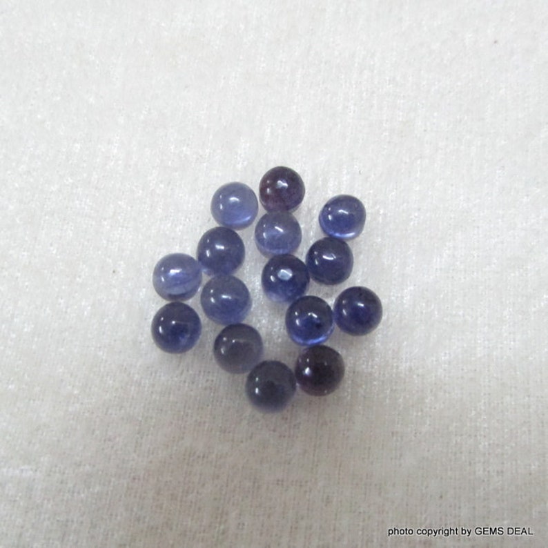 May include: A collection of 16 round, smooth, blue gemstones. The gemstones are scattered on a white, textured surface.