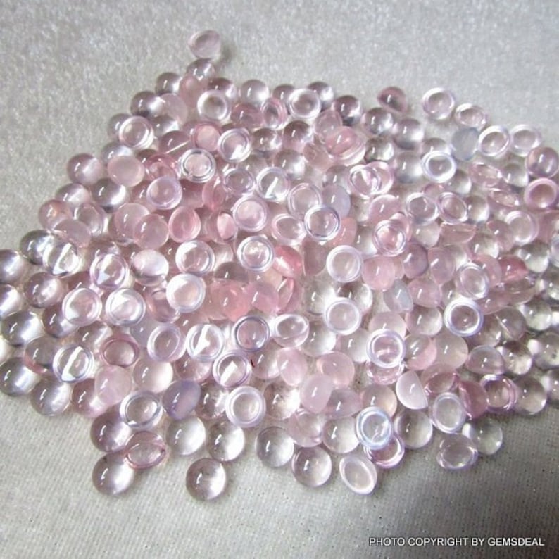 May include: A large pile of translucent pink cabochon gemstones. The stones are smooth and round, with a slight shimmer.