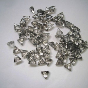 May include: A pile of clear quartz crystal points with black inclusions. The points are triangular in shape and have a shiny, translucent appearance.