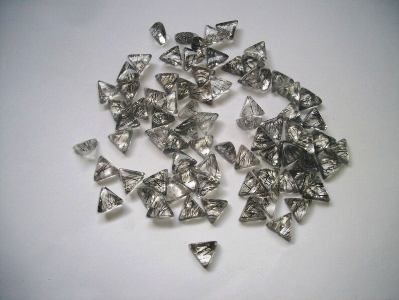 May include: A pile of clear quartz crystal points with black inclusions. The points are triangular in shape and have a shiny, translucent appearance.