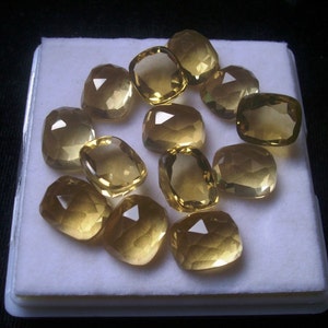 May include: A collection of 12 faceted, cushion-cut, yellow gemstones displayed on a white background.
