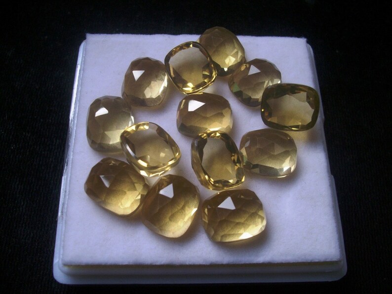 May include: A collection of 12 faceted, cushion-cut, yellow gemstones displayed on a white background.