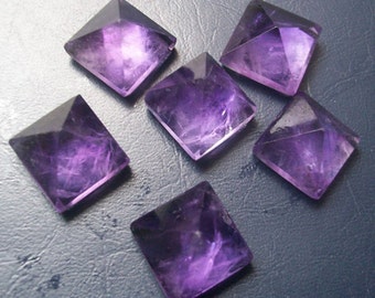 May include: Six purple amethyst crystal pyramids, each with a square base and a pointed top. The crystals are arranged on a dark gray surface.