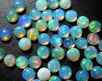 May include: A collection of iridescent opal gemstones. The opals are round, with a polished surface, and display a range of colours including blue, green, yellow, and white. The gemstones are scattered on a dark surface.