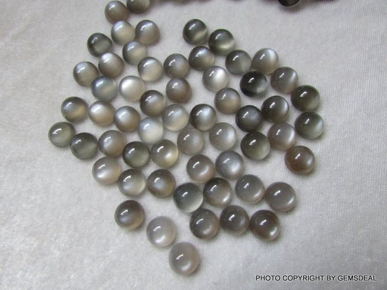 May include: A collection of 40 round, gray moonstone cabochons. The cabochons are smooth and have a subtle shimmer.