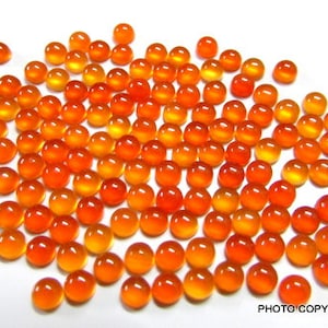 May include: A large group of round, orange and yellow cabochon gemstones. The stones are smooth and polished, and they have a translucent appearance.