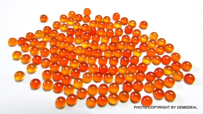 May include: A large group of round, orange and yellow cabochon gemstones. The stones are smooth and polished, and they have a translucent appearance.