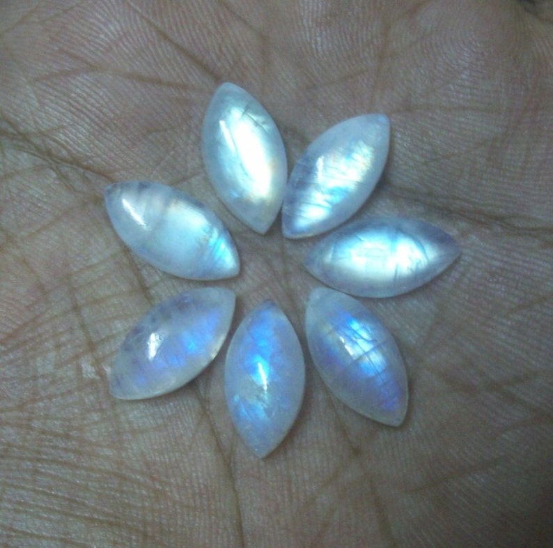 Puede incluir: Siete cabujones de piedra lunar blanca iridiscente en forma de marquesa, dispuestos en forma de flor.