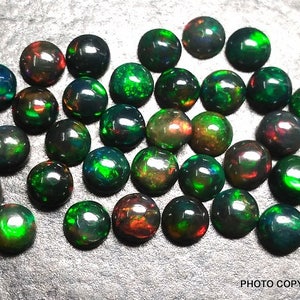 May include: A collection of 30 round black opal cabochons with green and red flashes. The opals are approximately 6mm in diameter.