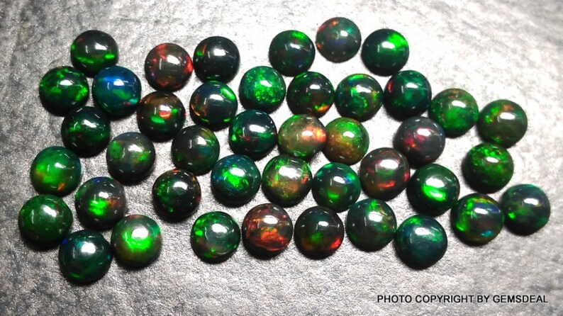 May include: A collection of 30 round black opal cabochons with green and red flashes. The opals are approximately 6mm in diameter.