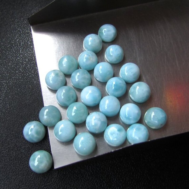 May include: A collection of light blue gemstone cabochons, arranged in a triangular pattern on a silver tray.
