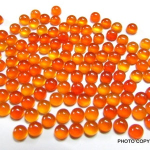 May include: A large group of round, orange and yellow carnelian cabochons. The cabochons are smooth and polished, with a slight sheen.