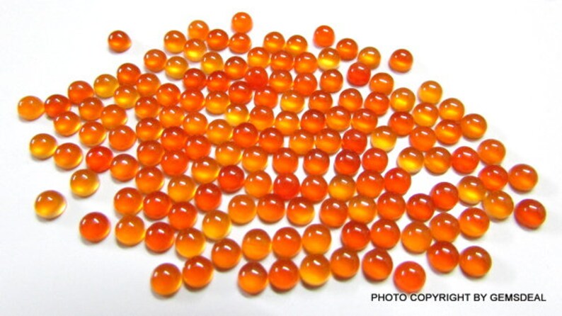 May include: A large group of round, orange and yellow carnelian cabochons. The cabochons are smooth and polished, with a slight sheen.