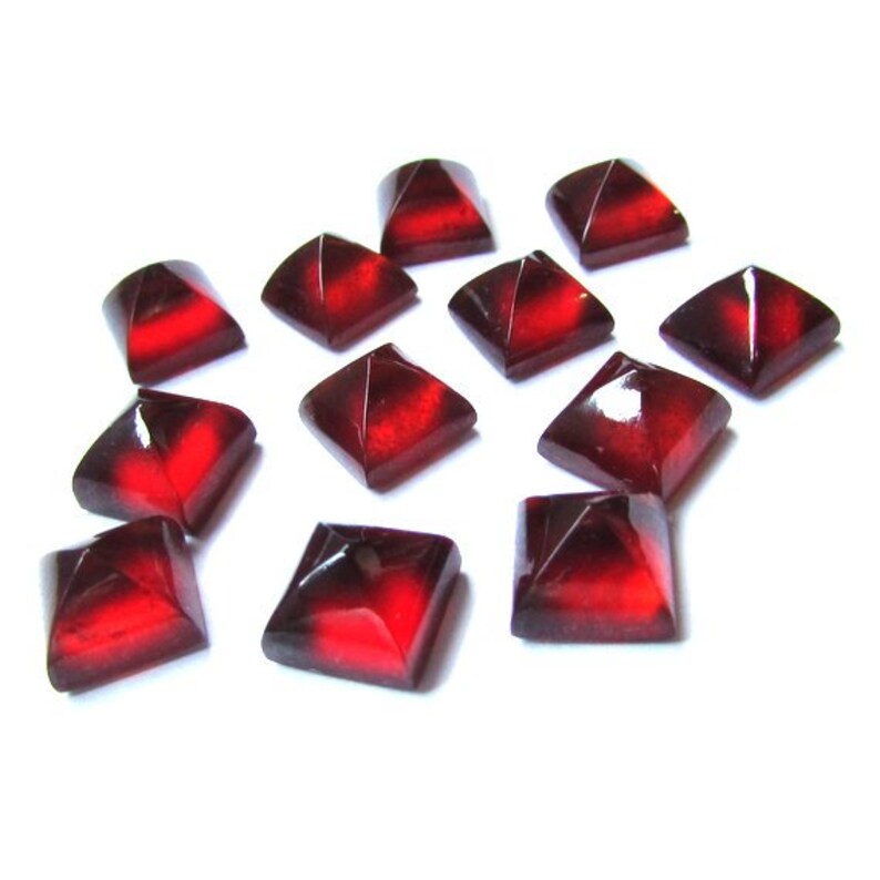 May include: A collection of square, faceted beads in shades of deep red and black. The beads are arranged on a white background, with light reflecting off their surfaces. The geometric shapes and color gradient create a striking visual effect.