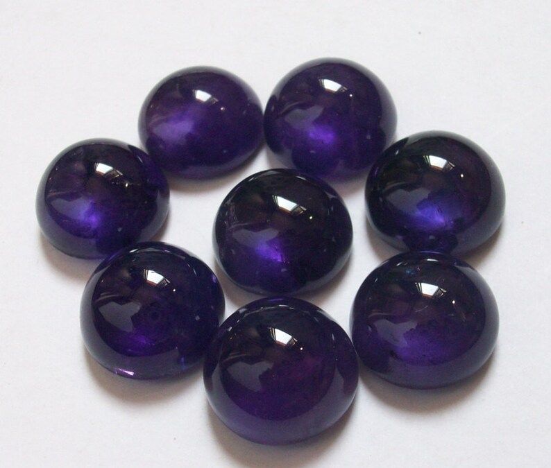 May include: Eight round, purple cabochon gemstones. The gemstones are smooth and shiny.