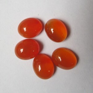 May include: Five oval-shaped carnelian gemstones, each with a smooth, polished surface and a vibrant orange color.