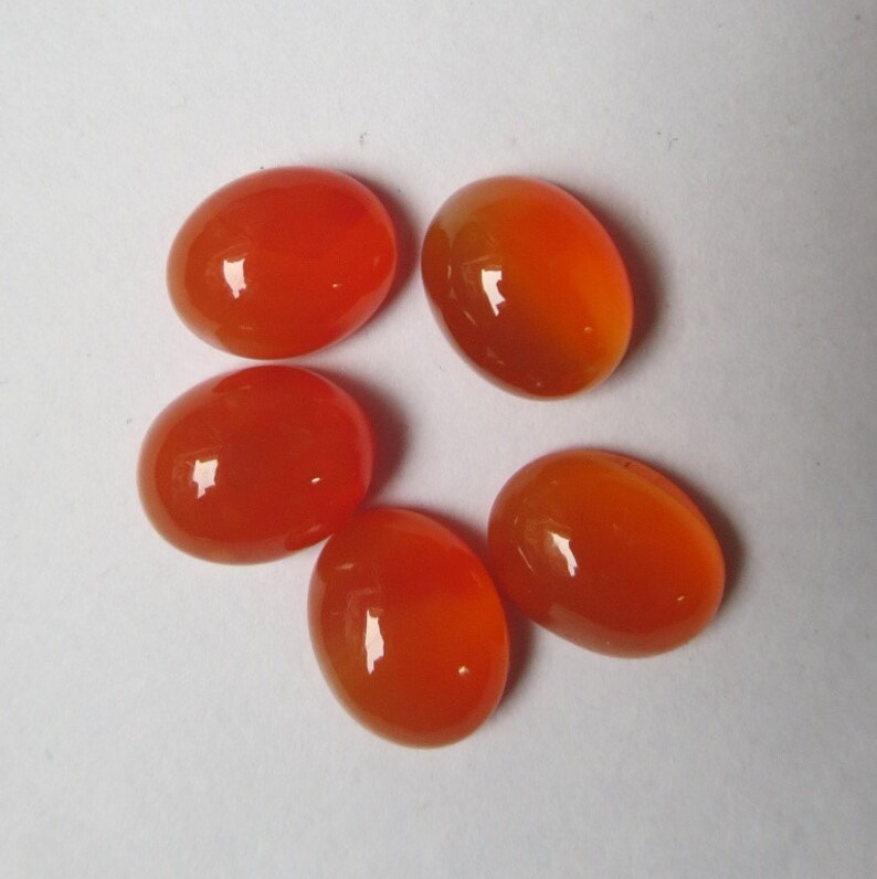 May include: Five oval-shaped carnelian gemstones, each with a smooth, polished surface and a vibrant orange color.