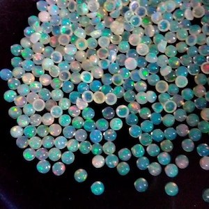 May include: A large group of iridescent opal cabochons in various shades of blue, green, and white. The cabochons are round and have a smooth, polished surface.