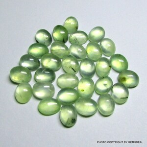 May include: A collection of 30 oval-shaped green gemstones. The stones are smooth and polished, with a translucent appearance.