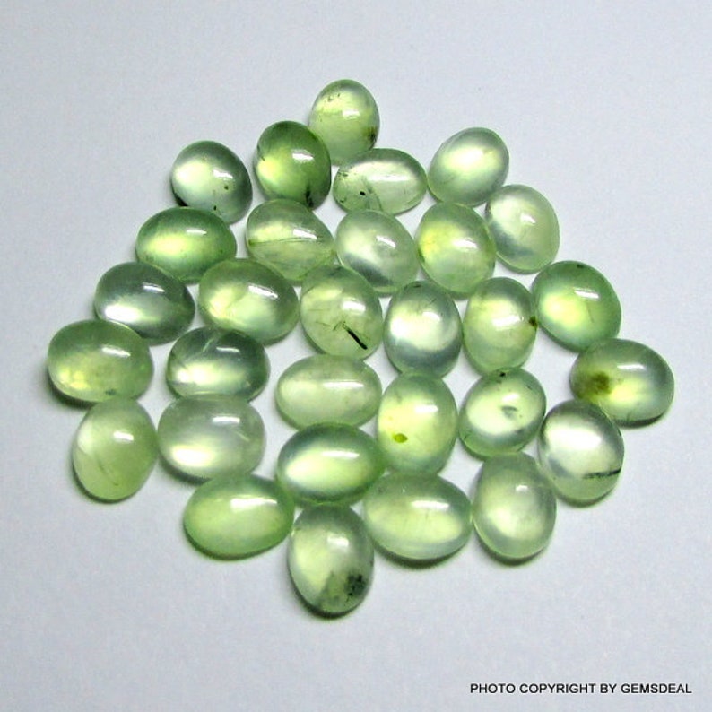 May include: A collection of 30 oval-shaped green gemstones. The stones are smooth and polished, with a translucent appearance.