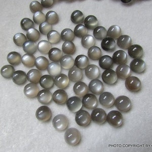 May include: A collection of 40 round, gray moonstone cabochons. The stones are smooth and have a subtle shimmer.