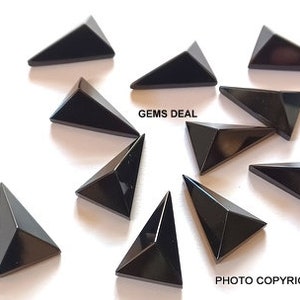 Può includere: Dieci cabochon di pietra preziosa triangolari neri, ognuno con una punta appuntita, disposti su una superficie bianca. Il testo "GEMS DEAL" è visibile nell'immagine.