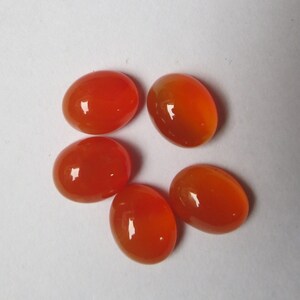 May include: Five oval-shaped carnelian gemstones in various shades of orange. The stones are smooth and polished, with a glossy finish.